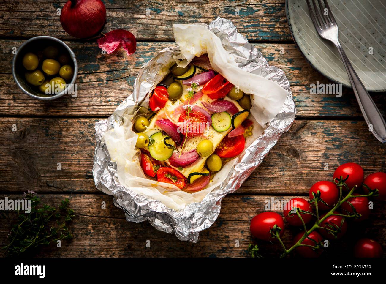 Feta mit Tomaten, Zucchini, Oliven, Zwiebeln und Thymian in Pergamentpapier Stockfoto