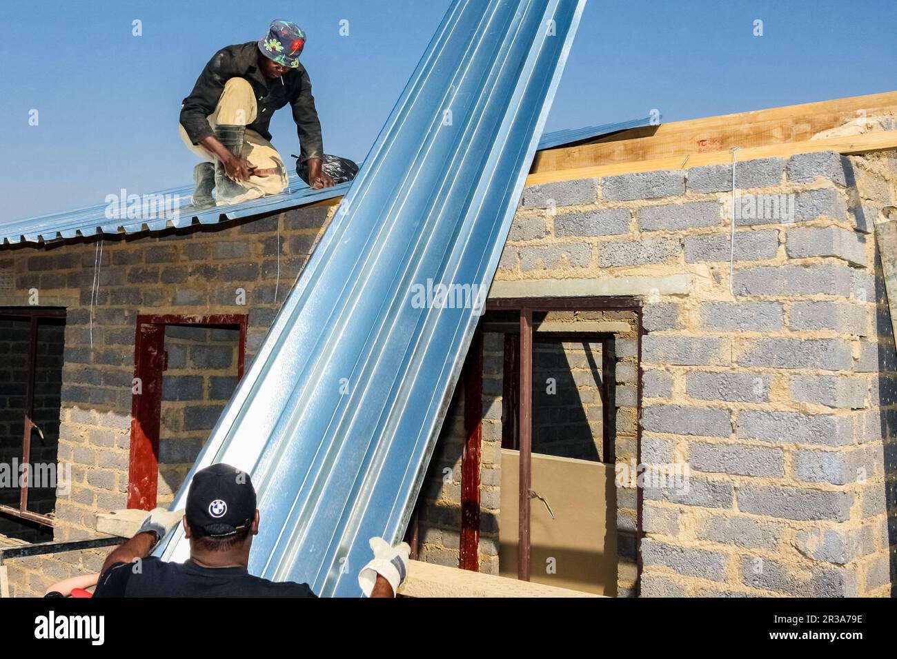 Vielfältiges Community Outreach-Programm, das bei der Installation von Metalldächern in einem kleinen, erschwinglichen Haus in einer lokalen Gemeinde hilft Stockfoto