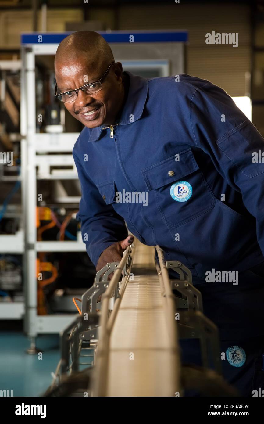 Schwarzer afrikanischer Vorgesetzter, der eine Maschine an einer Montagelinie einer Verpackungsfabrik überprüft Stockfoto
