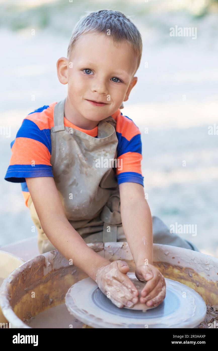 Ein kleiner lächelnder Junge, produziert auf Töpferrad-Topf. Hände eines jungen Töpfchens, der ein Erdenglas kreiert Stockfoto