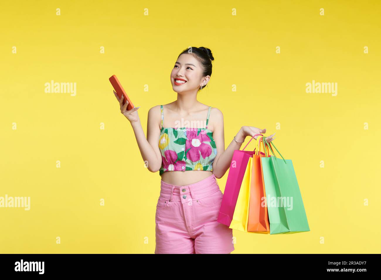 Schöne, attraktive Asiatin, die Einkaufstaschen und Handy über dem Spielplatz hält Stockfoto