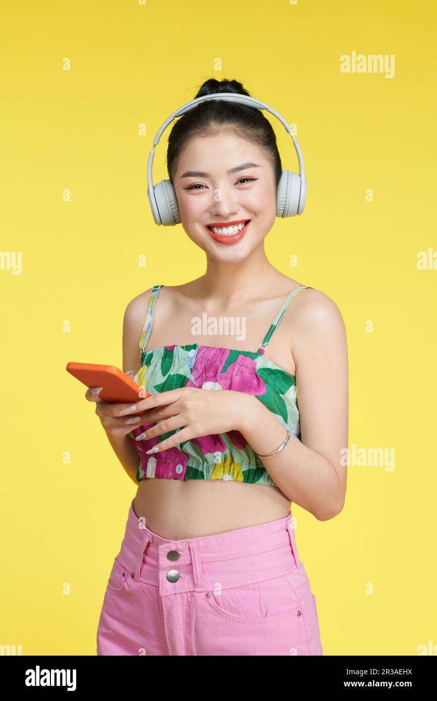Fröhliche, nette Frau mit Kopfhörern, moderne Technologie, die in der Nähe leerer Räume mit Telefon steht Stockfoto