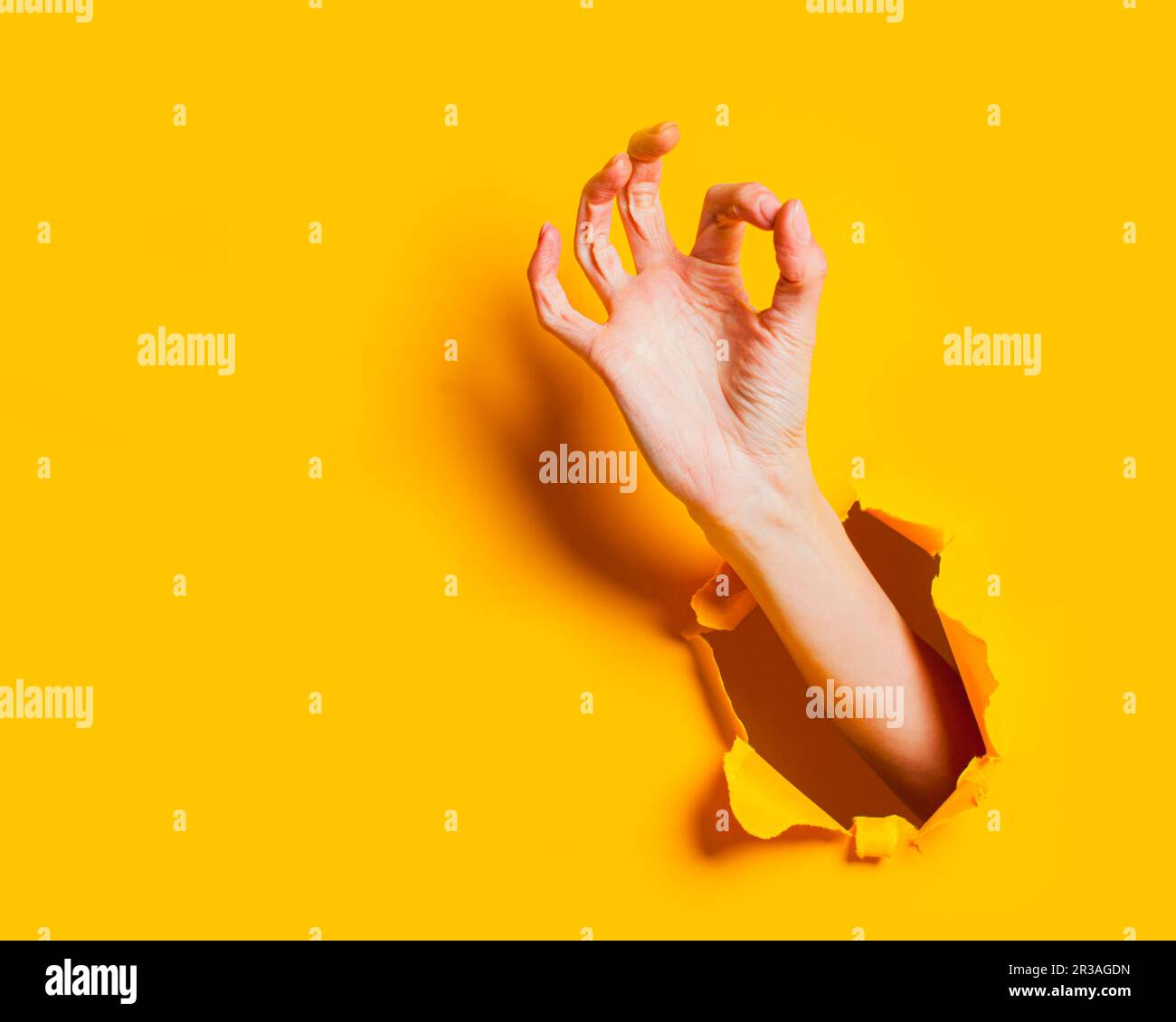 Hand macht okay Geste durch Löcher auf gelbem Hintergrund. Stockfoto