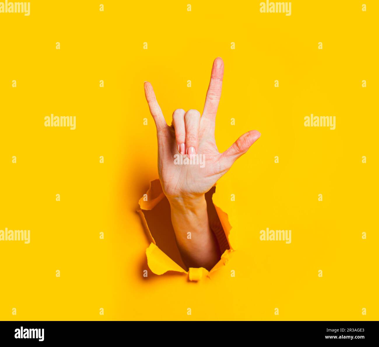 Weibliche Hand macht Rock and Roll Geste durch Loch in gelbem Papier. Stockfoto
