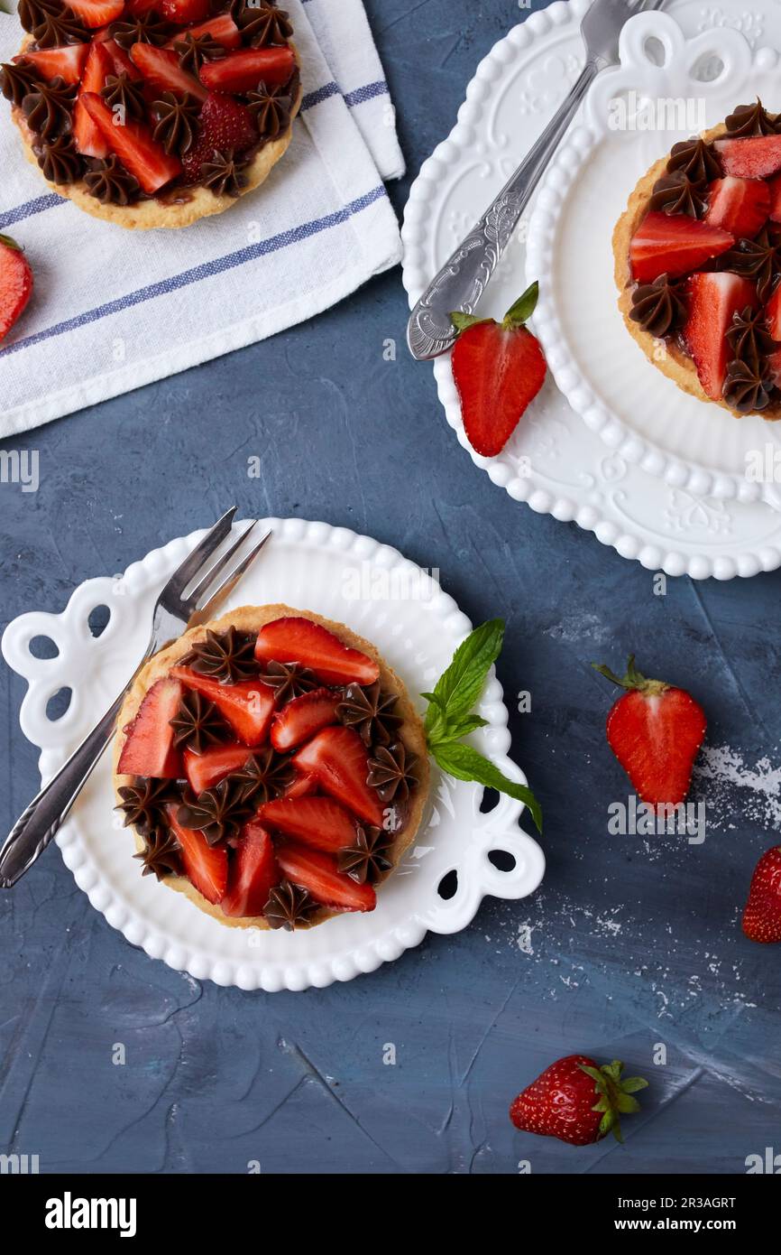 Minitarte mit Erdbeermarmelade, serviert mit frischen Erdbeeren und Schokoladenganache Stockfoto