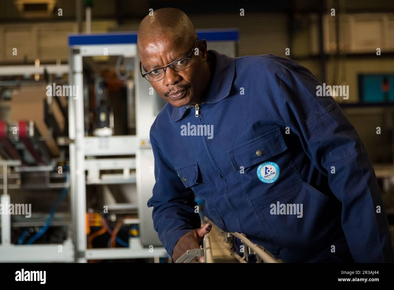 Schwarzer afrikanischer Vorgesetzter, der eine Maschine an einer Montagelinie einer Verpackungsfabrik überprüft Stockfoto