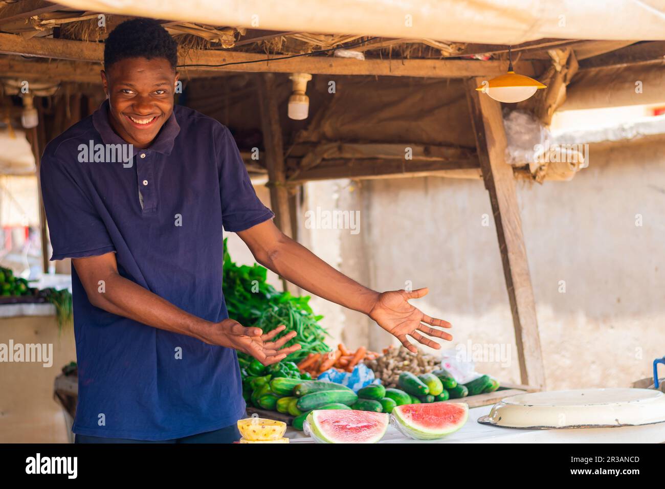 Bild eines jungen afrikanischen Händlers, der Gemüse und andere Früchte auf einem typischen afrikanischen Markt zeigt. Stockfoto