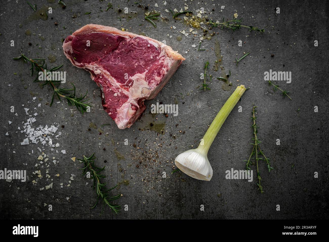 Rohes T-Bone-Steak, Rosmarin, Thymian, halbierte Knoblauchknolle, Gewürze und Meersalz Stockfoto