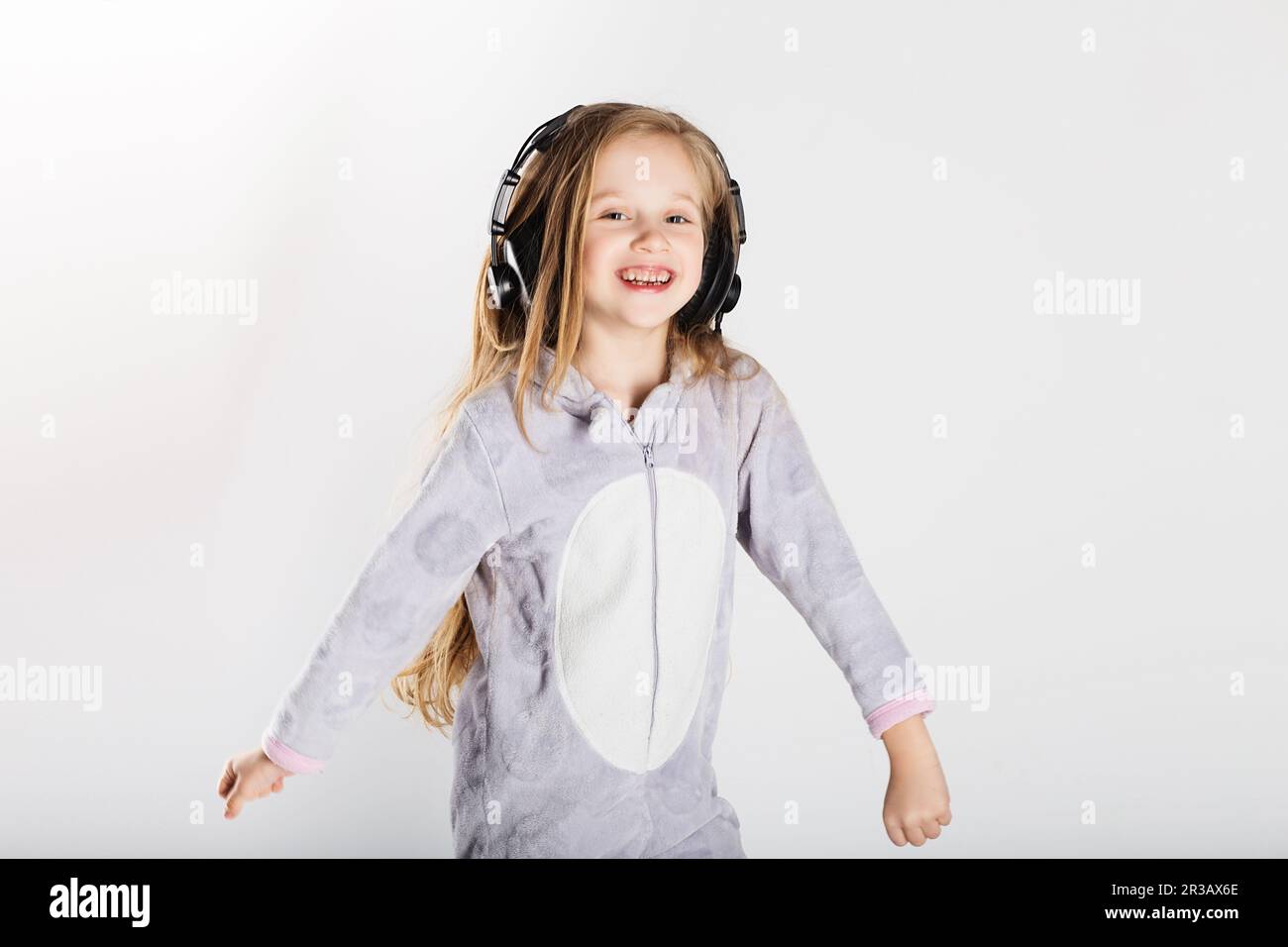 Das süße kleine Mädchen mit Kopfhörern benutzt ein Smartphone, schaut in die Kamera und hat zu Hause Spaß. Tag Stockfoto