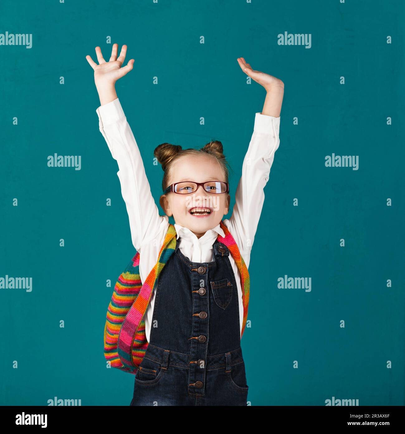 Lustiges, lächelndes kleines Mädchen mit großem Rucksack, das springt und Spaß an der blauen Wand hat. Ich schaue auf Cam Stockfoto