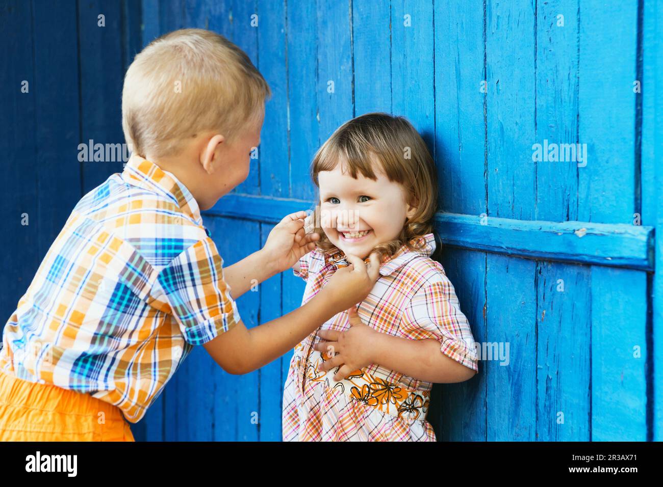 Bruder kitzelt ihre Schwester. Kleine Kinder spielen gegen blaue Holzwand Stockfoto