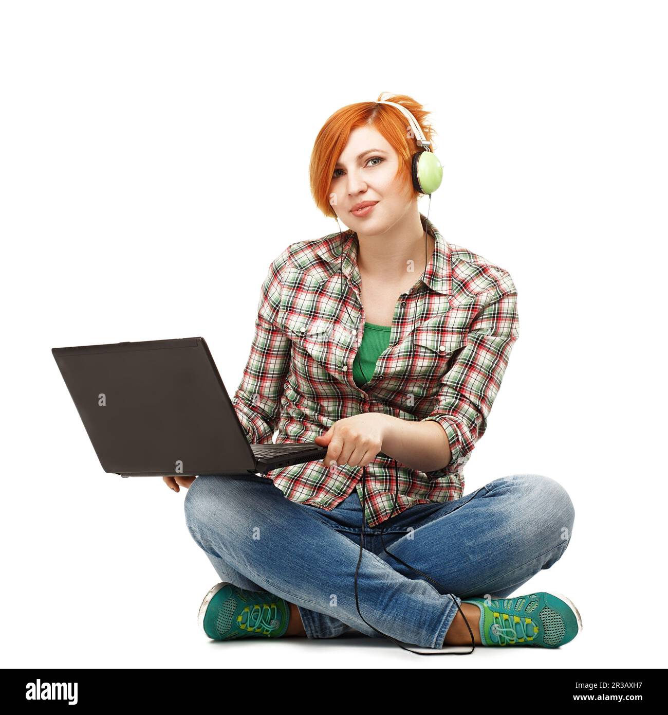 Ein junges, schönes Mädchen mit einem Laptop, das Musik über Kopfhörer hört, isoliert auf weißem Backg Stockfoto