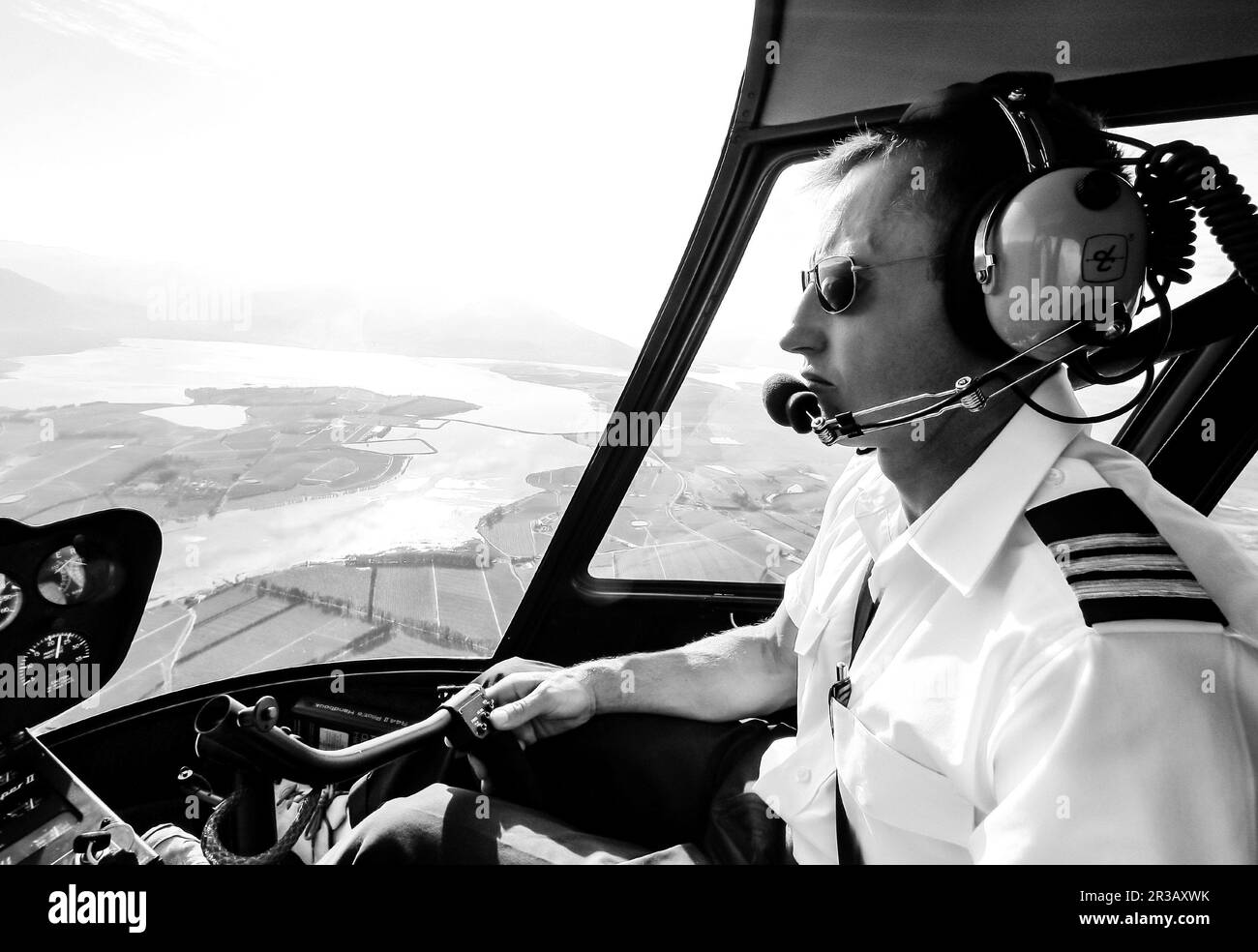 Männlicher, weißer Hubschrauberpilot, der einen Hubschrauber vom Typ R44 über dem Land fliegt Stockfoto
