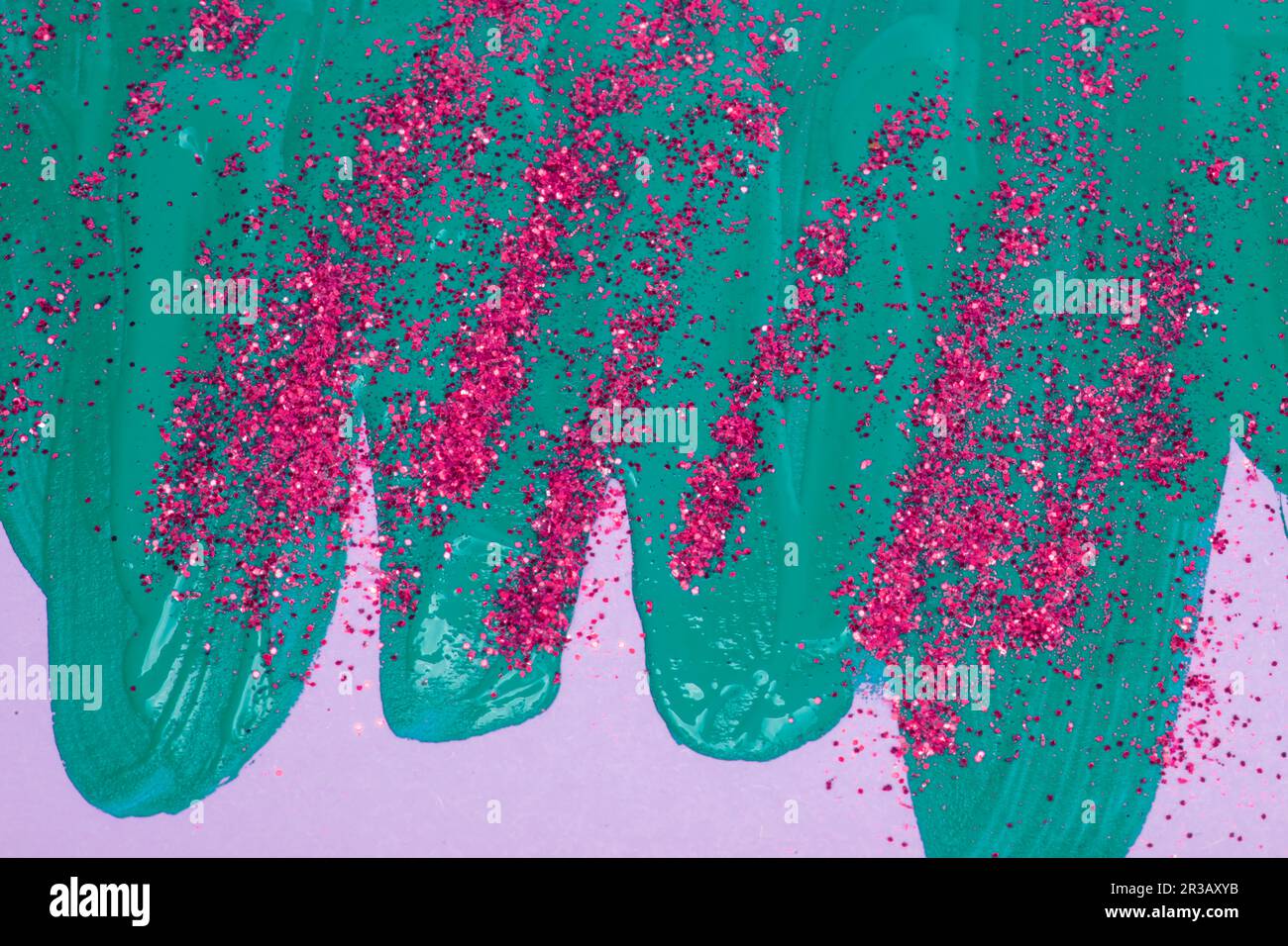 Auf einem rosafarbenen Hintergrund sind blaue schillernde Flecken von fließender Acrylfarbe mit pinkfarbenen Glitzern zu sehen. Stockfoto