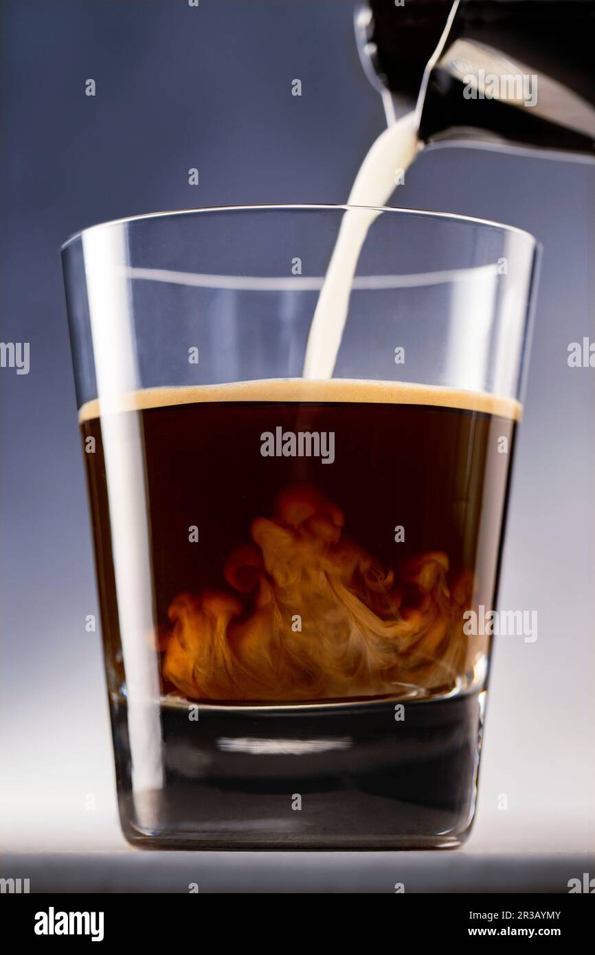 Milch wird mit Espresso in ein Glas gegossen Stockfoto