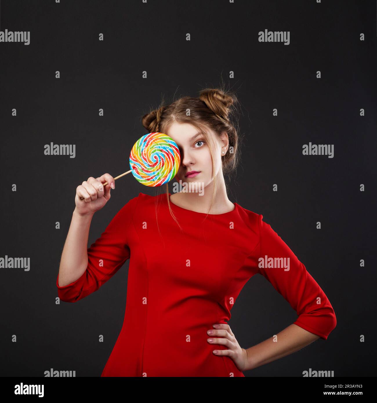 Portrait eines lächelnden jungen, wunderschönen Mädchens in einem roten Kleid mit großen Süßigkeiten. Komisches Mädchen mit einem Lollip Stockfoto