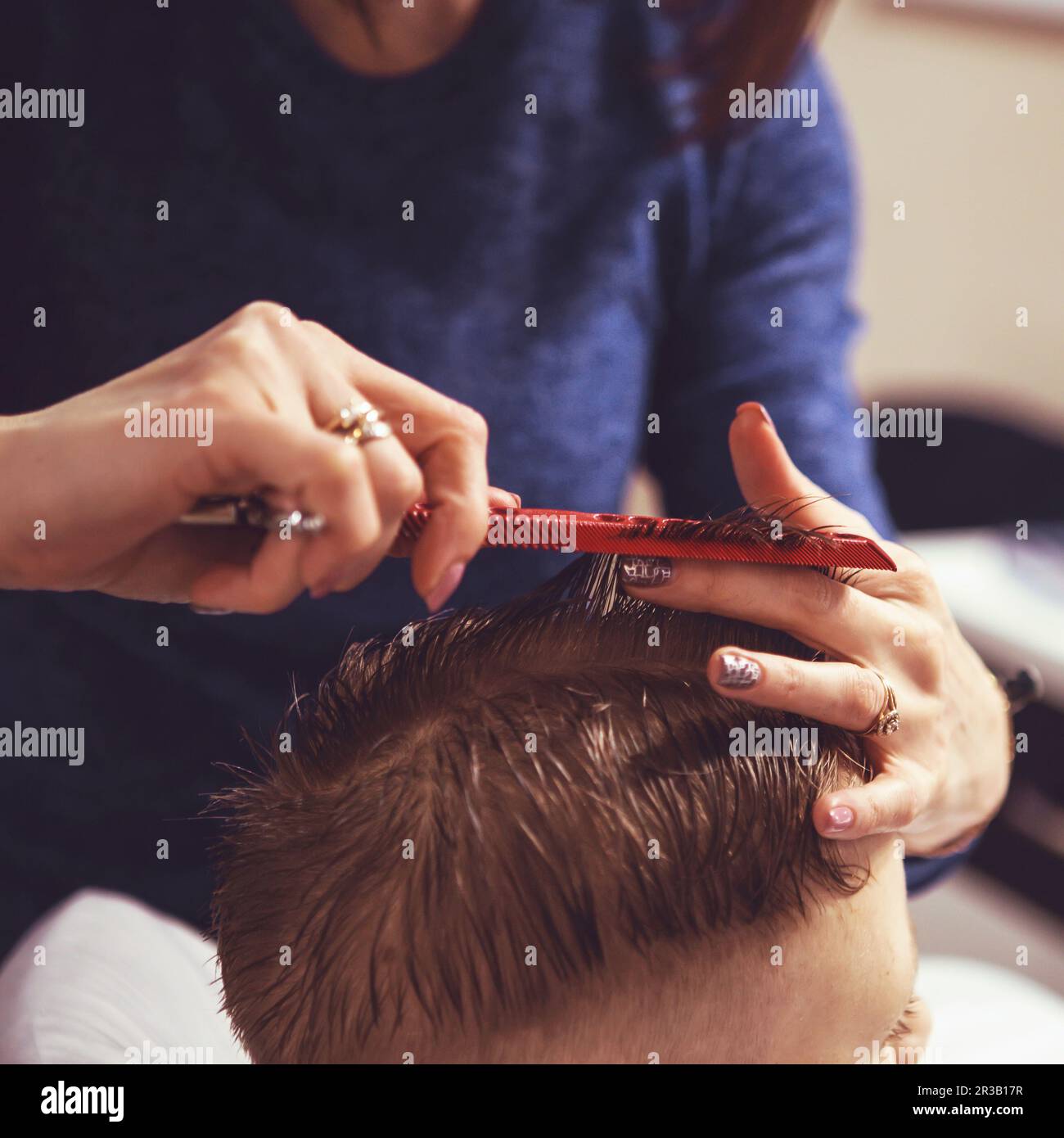 Kleiner Junge beim Friseur. Das Kind hat Angst vor Haarschnitten. Friseurhände, die Frisuren machen Stockfoto