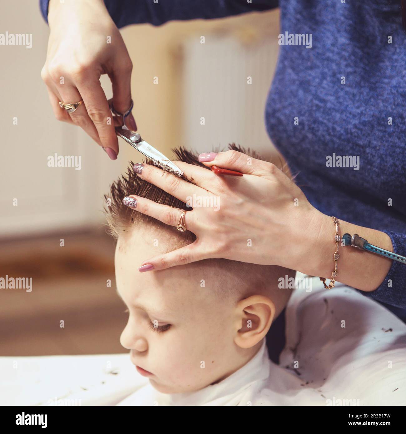 Kleiner Junge beim Friseur. Das Kind hat Angst vor Haarschnitten. Friseurhände, die Frisuren machen Stockfoto