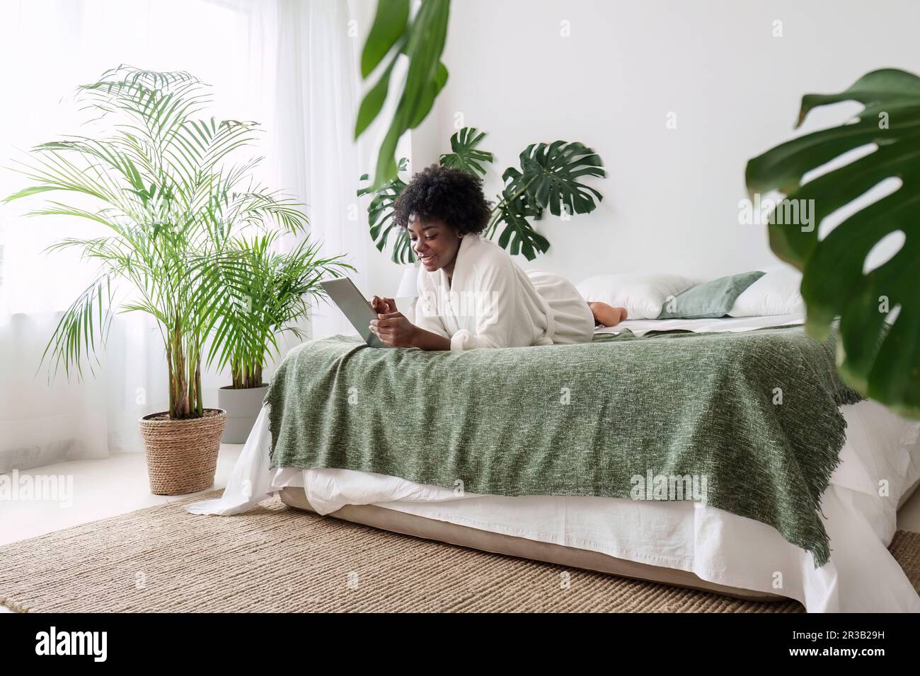 Frau, die einen Tablet-PC benutzt und in einem umweltfreundlichen Zuhause auf dem Bett liegt Stockfoto