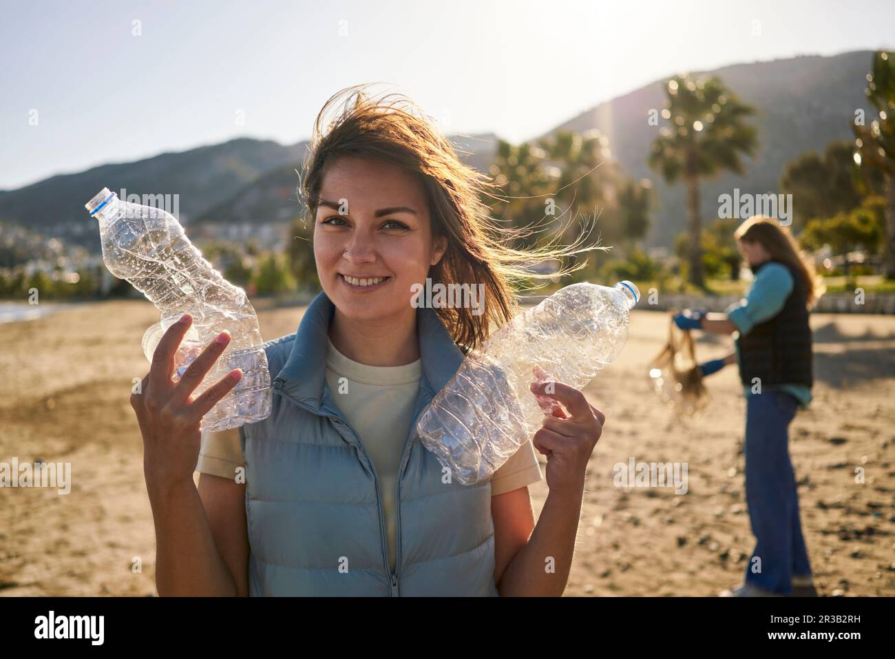 Lächelnde Frau mit zerknitterten Plastikflaschen am Strand Stockfoto