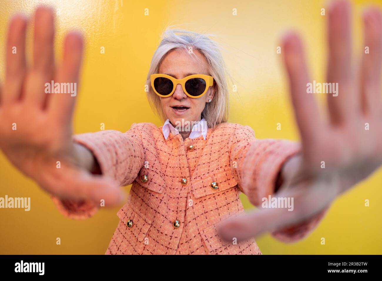 Eine Frau mit Sonnenbrille, die vor der gelben Wand stoppt Stockfoto