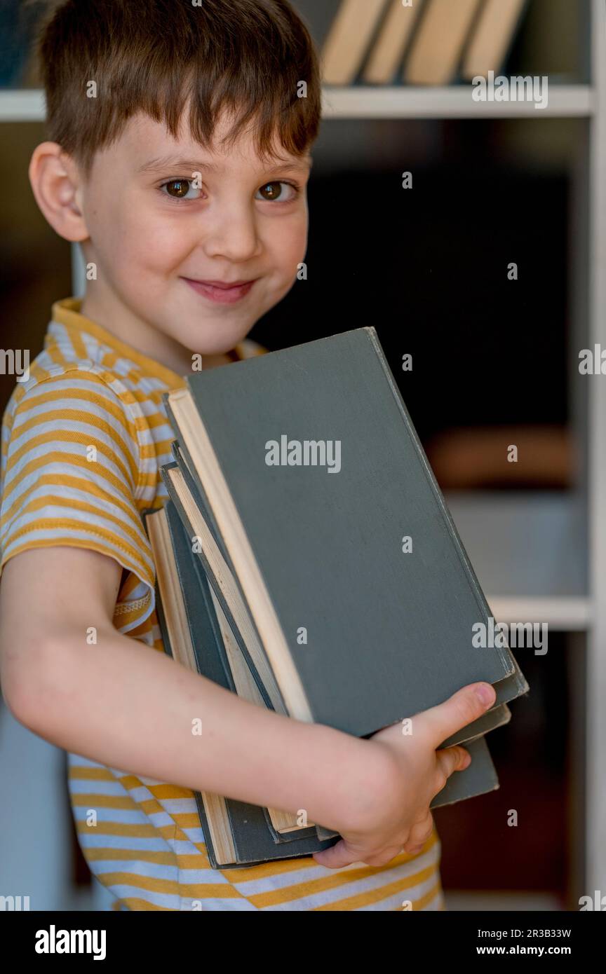 Ein lächelnder Junge, der zu Hause einen Stapel Bücher in der Hand hat Stockfoto