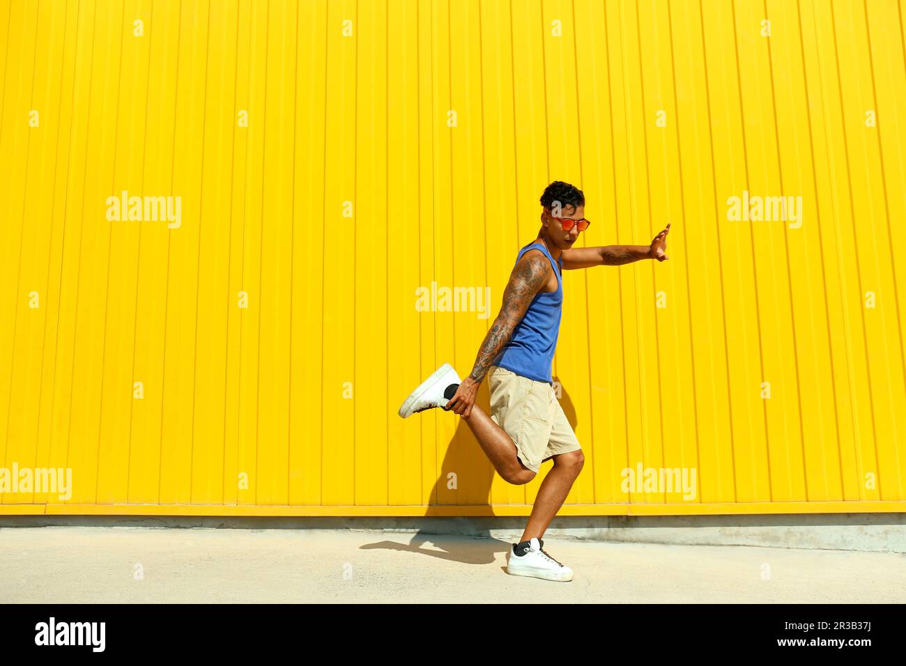 Ein Mann, der an sonnigen Tagen Tanzbewegungen vor der gelben Wand zeigt Stockfoto