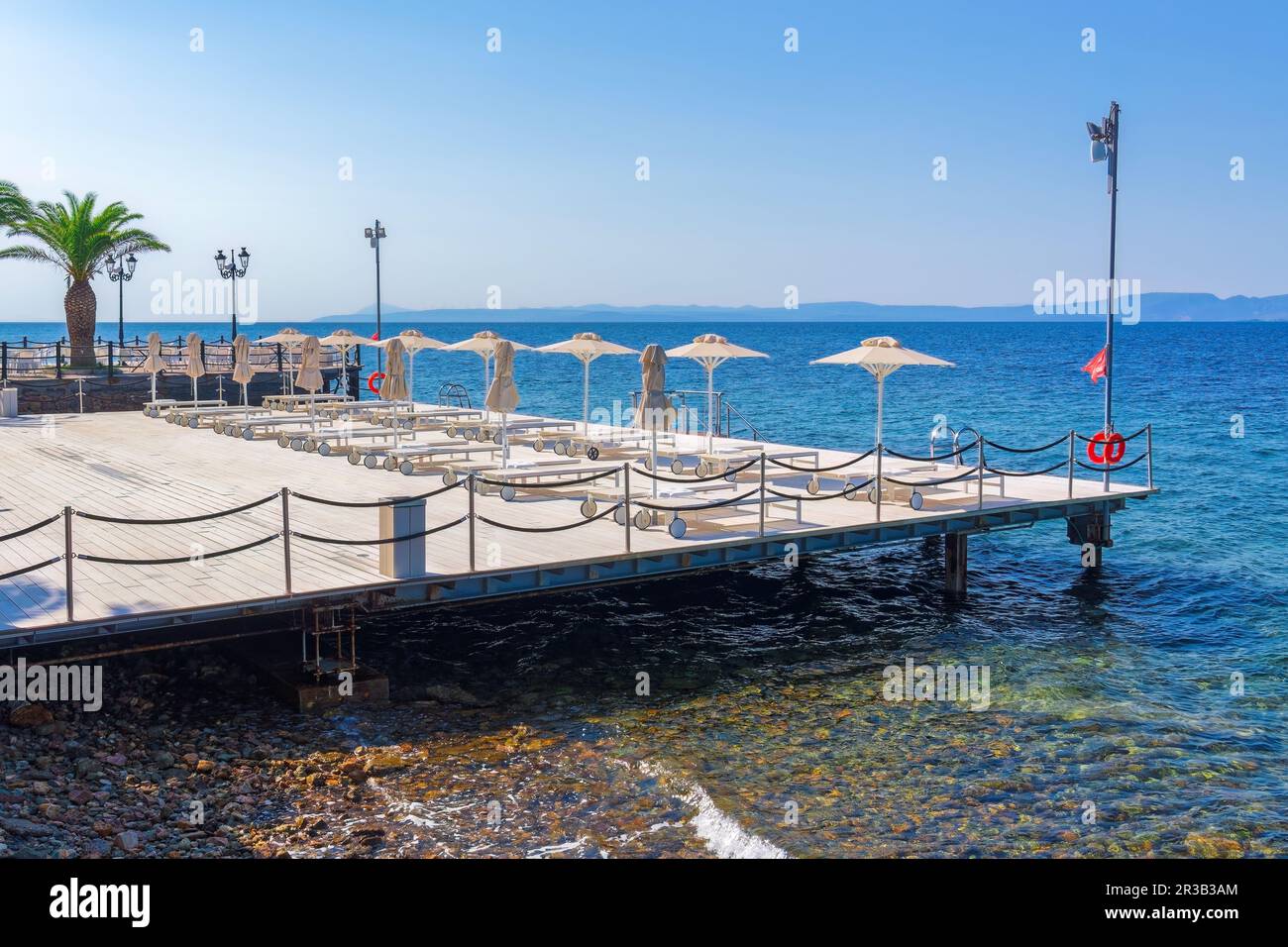 Leere Holzsonnendeck mit Stühlen und Sonnenschirmen am ruhigen blauen Meer unter der hellen Sonne im Sommer. Stockfoto