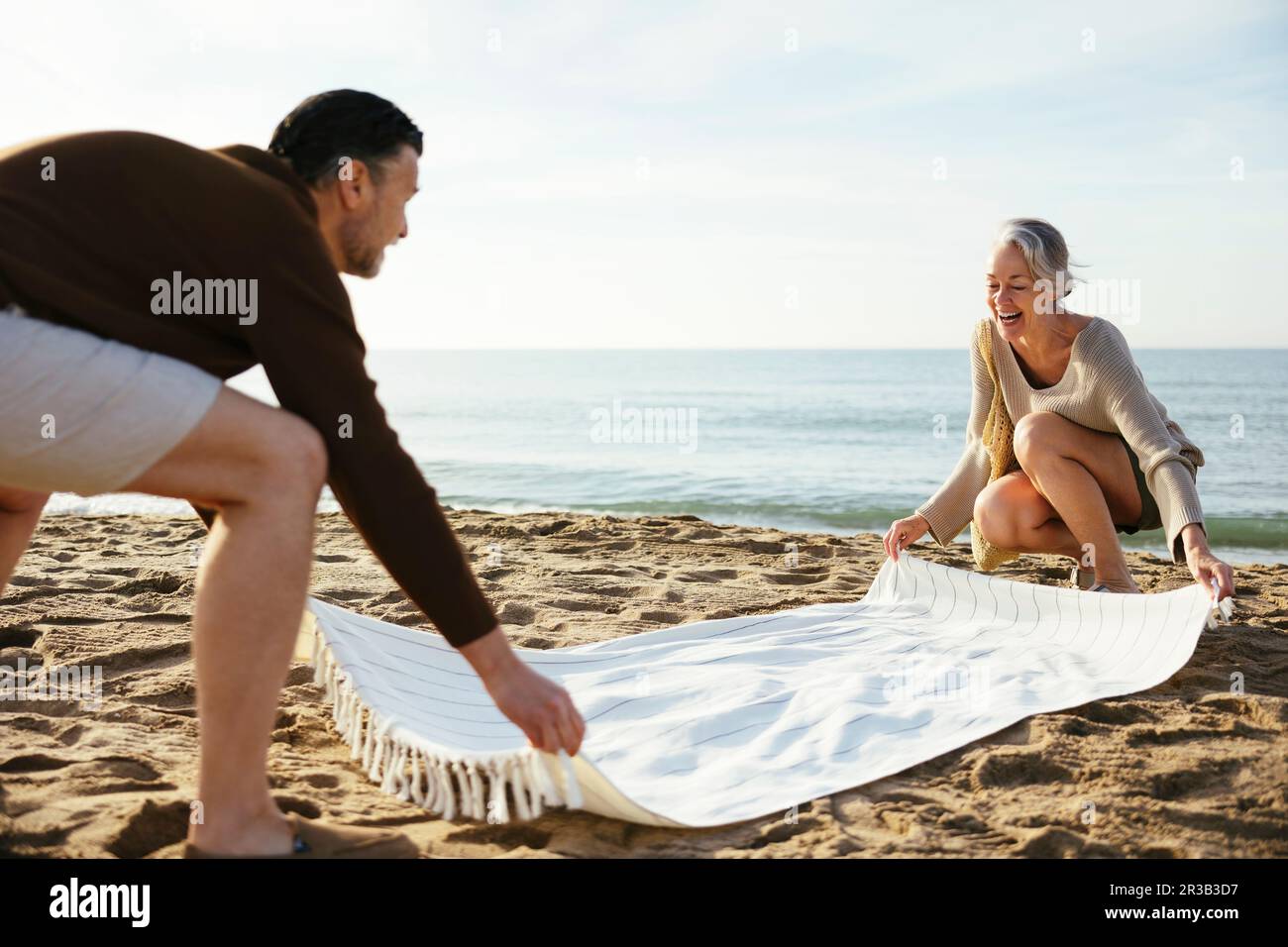 Glückliches Paar, das am Strand eine Decke auf Sand streut Stockfoto