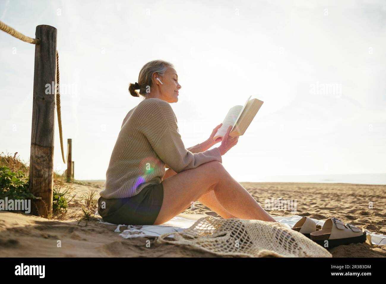 Reife Frau, die am sonnigen Tag am Strand Buch liest Stockfoto