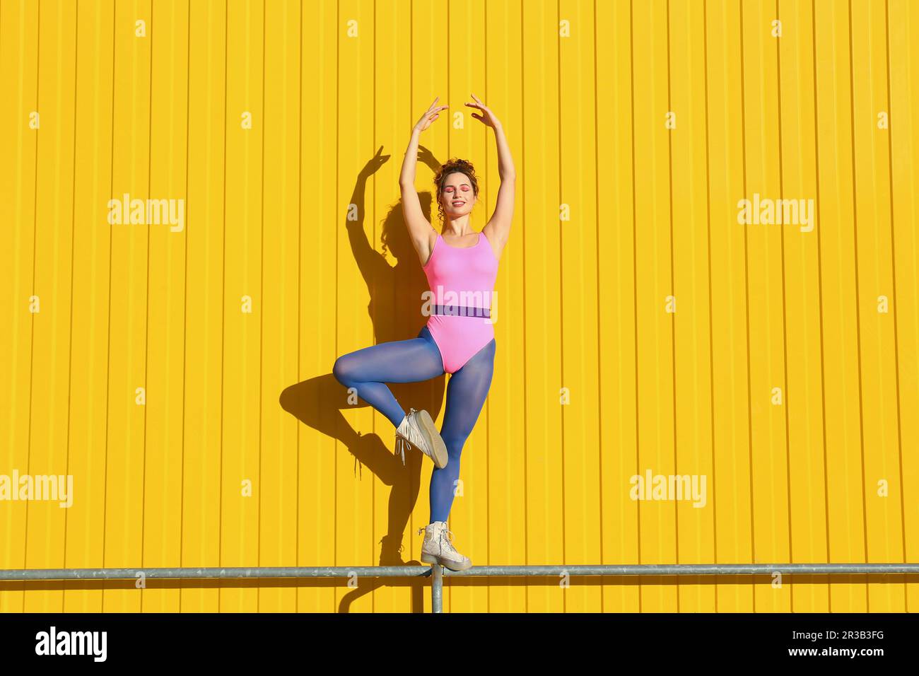 Junge Frau, die einen Body trägt und Ballett am Geländer vor der gelben Wand übt Stockfoto