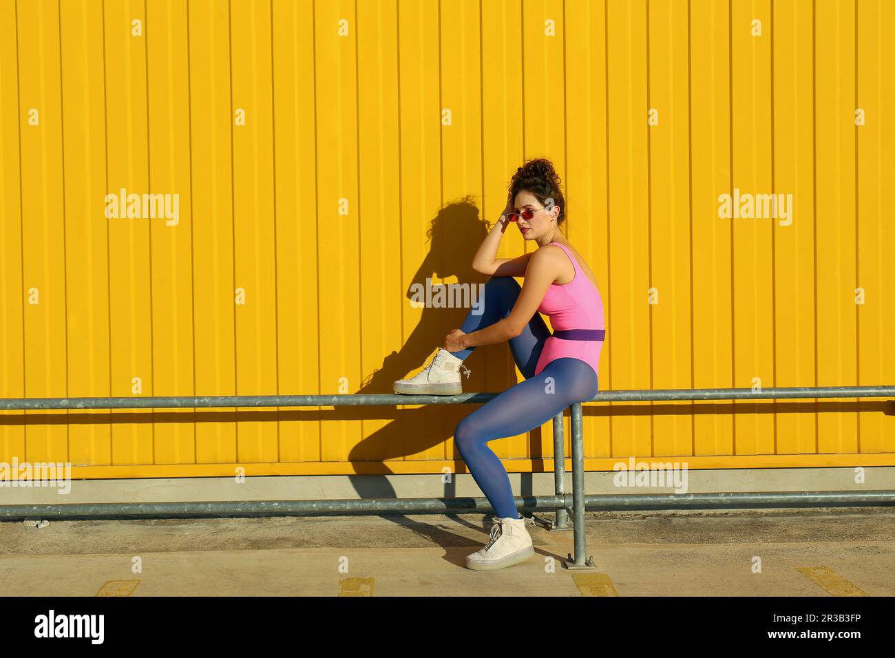 Eine Frau, die auf einem Geländer vor der gelben Wand sitzt Stockfoto