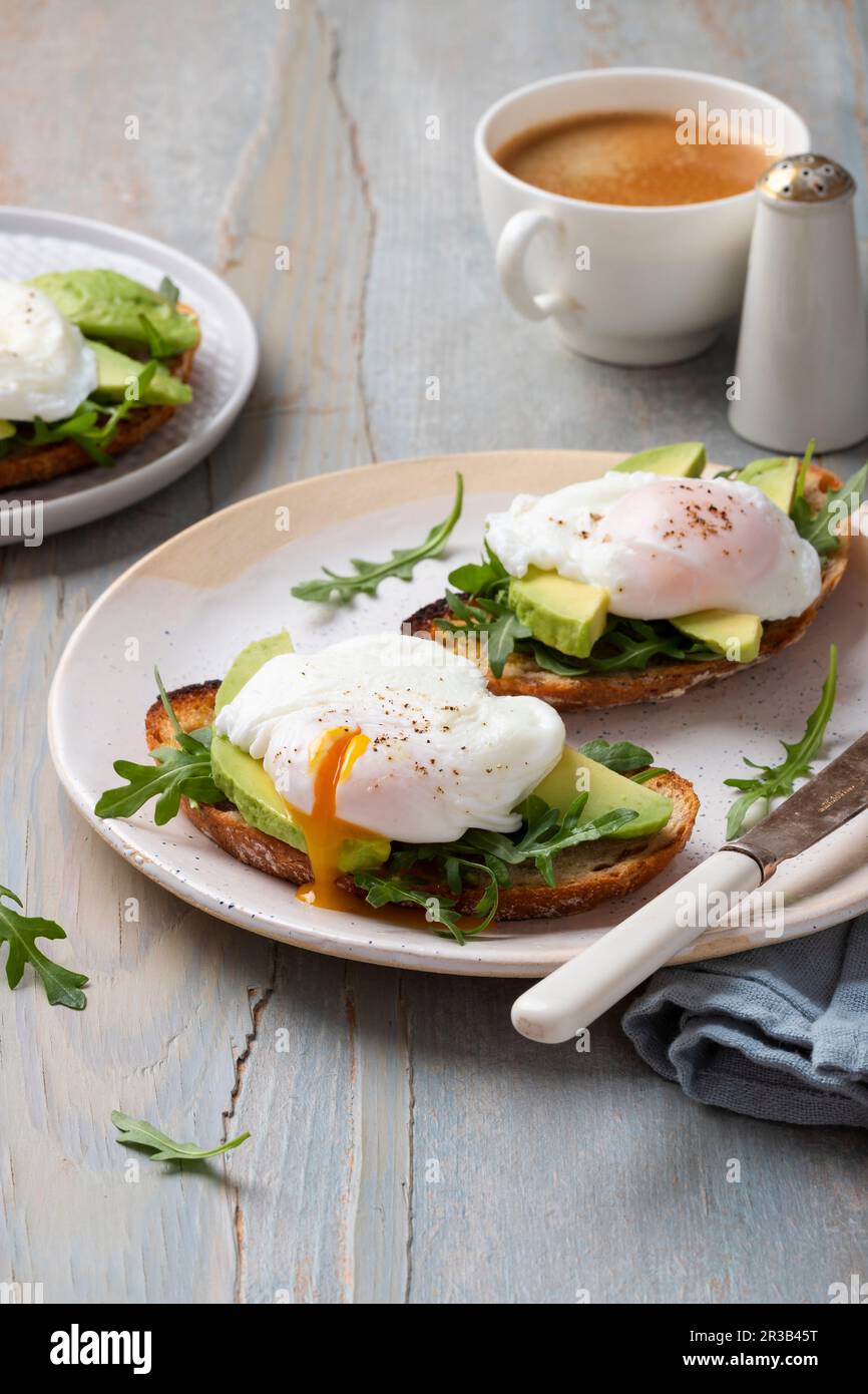 Toasts mit Avocado, Rucola und pochierten Eiern, Kaffee, Rucolablättern Stockfoto
