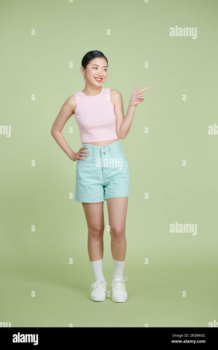 Junge Asiatin lacht, während sie mit dem Finger zur Seite zeigt, isoliert auf grünem Hintergrund Stockfoto