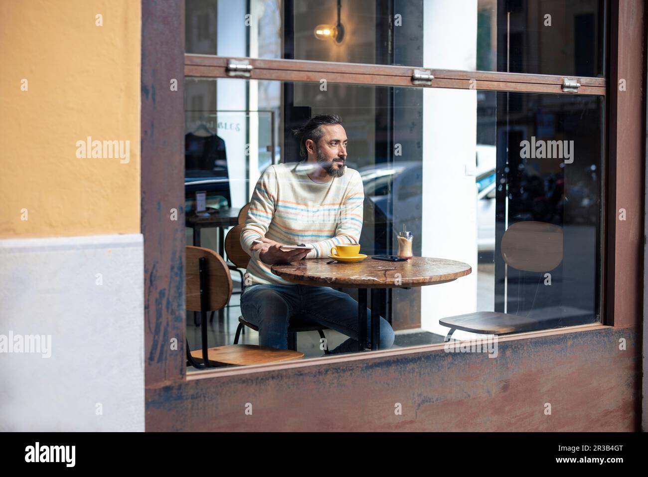 Ein denkwürdiger Mann, der im Café sitzt und durch ein Glasfenster gesehen wird Stockfoto