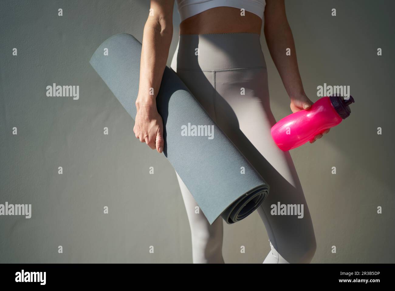 Eine Frau, die Yoga-Matte und Wasserflasche vor der Wand hält Stockfoto