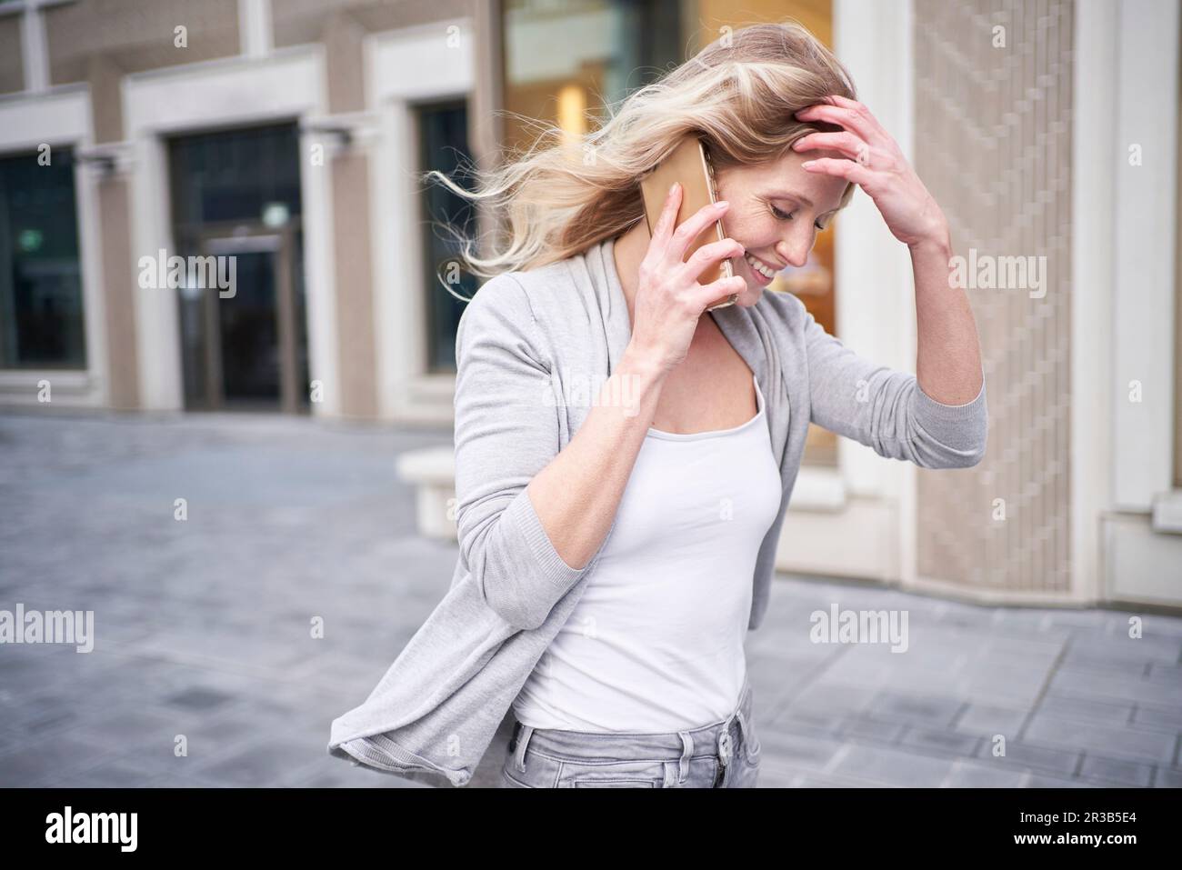Eine blonde Frau mit einer Hand im Haar, die mit einem Handy spricht Stockfoto