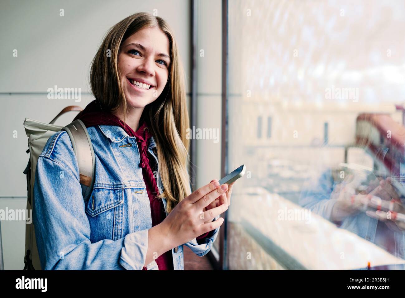 Lächelnde junge Frau, die am Flughafen ein Smartphone hält Stockfoto