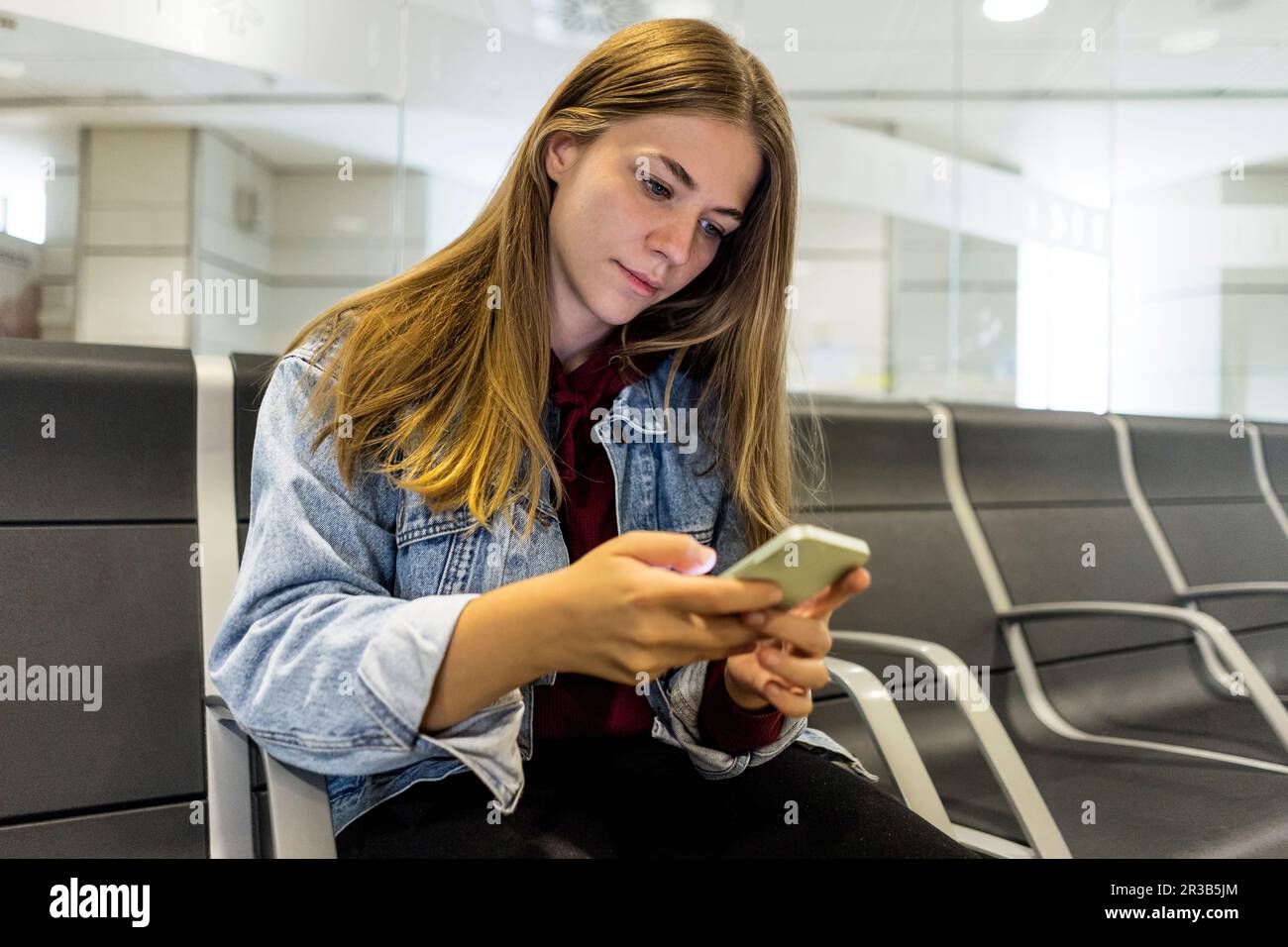 Junge Frau, die in der Lobby des Flughafens SMS über ein Smartphone schickt Stockfoto