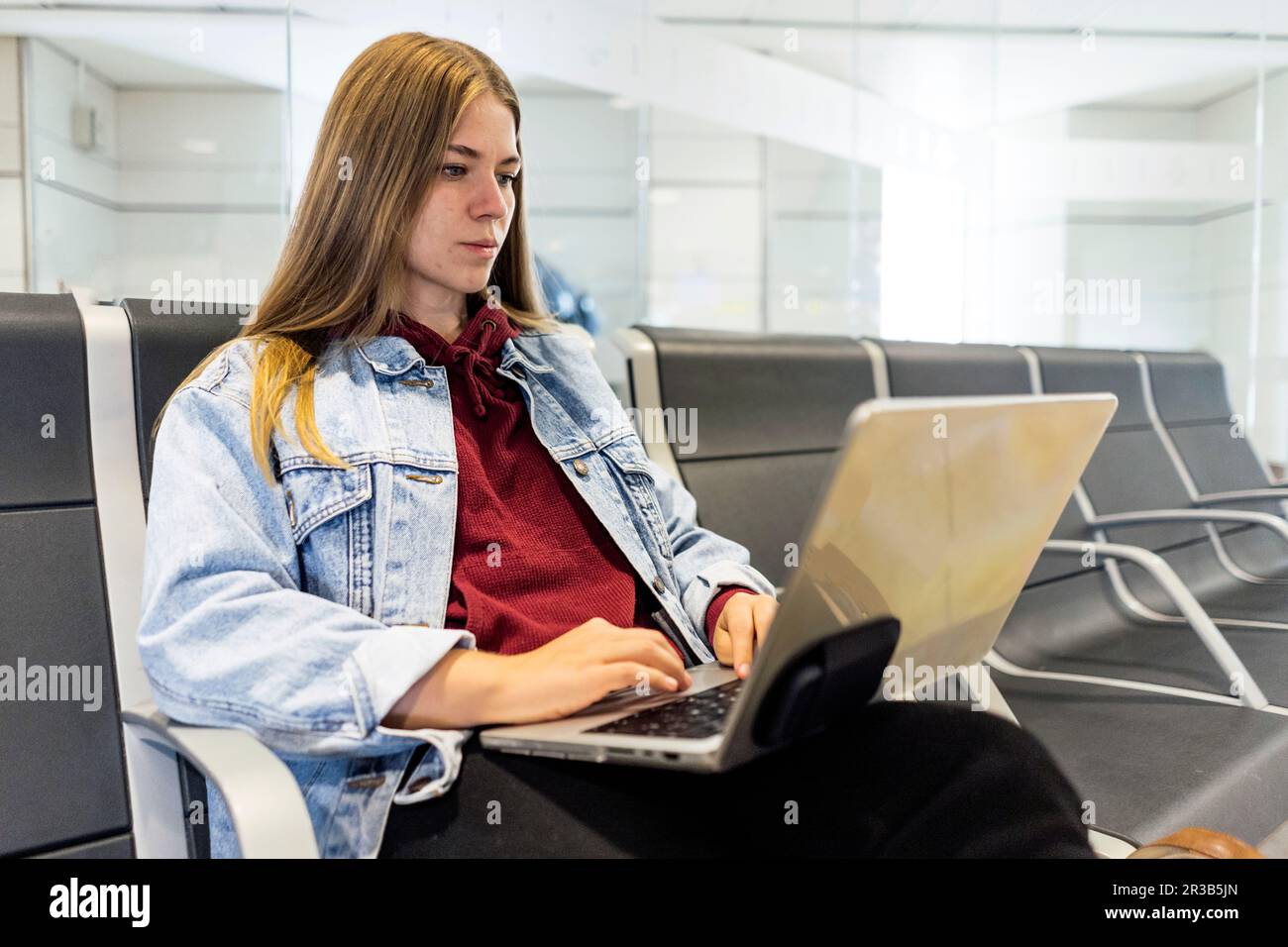 Junge Frau, die in der Flughafenlobby ein Notebook benutzt Stockfoto