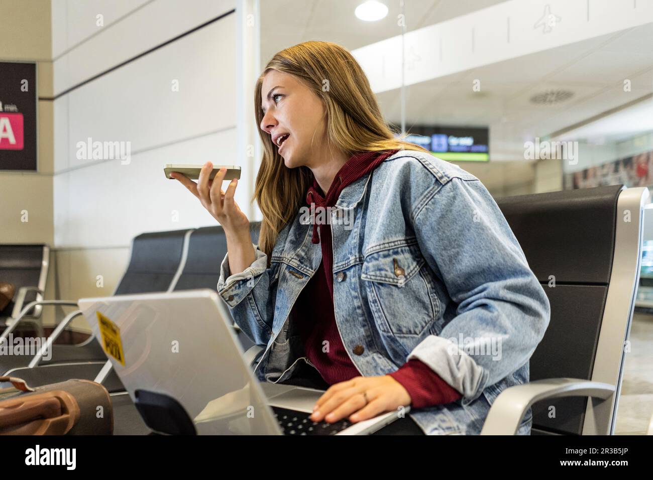 Junge Frau, die in der Flughafenlobby über Lautsprecher telefoniert Stockfoto