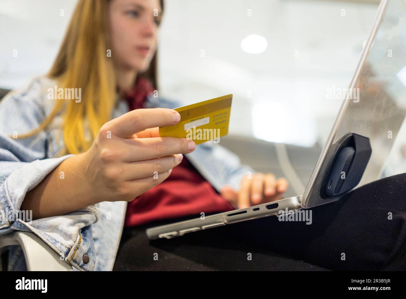 Junge Frau, die online mit Kreditkarte und Laptop in der Flughafenlobby einkauft Stockfoto