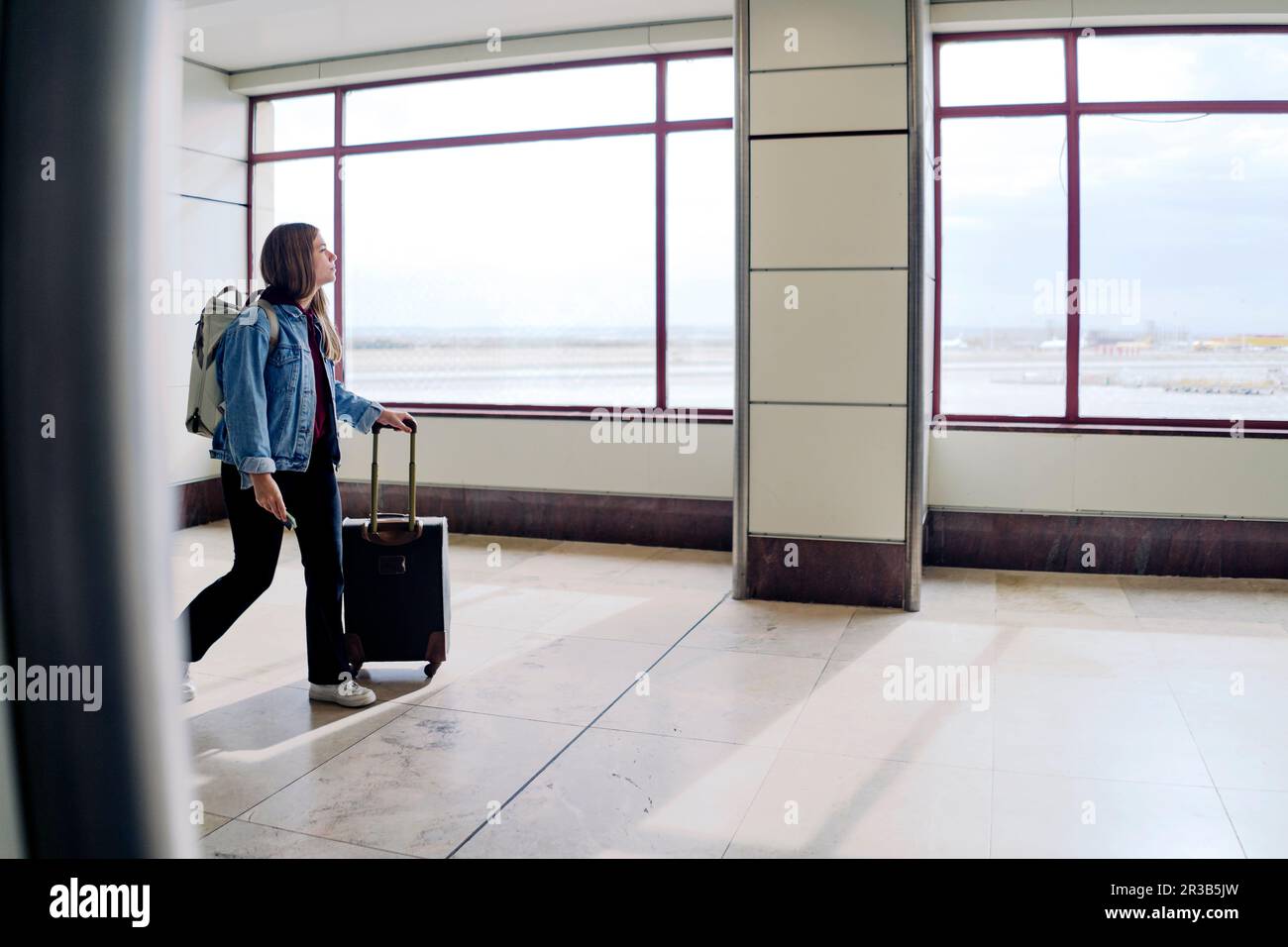 Junge Frau mit Koffer, die in der Flughafenlobby herumläuft Stockfoto