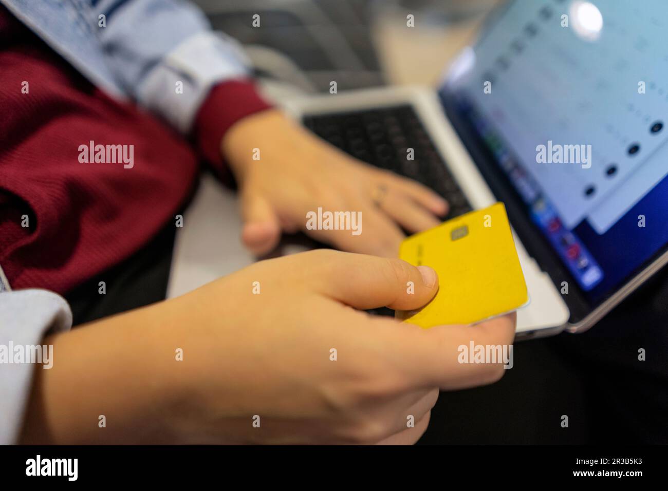 Junge Frau, die online mit Kreditkarte und Laptop in der Flughafenlobby einkauft Stockfoto