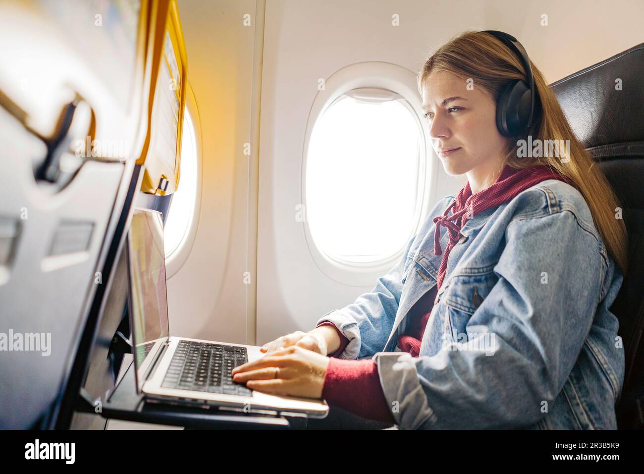 Eine junge Frau, die im Flugzeug Musik hört und ein Notebook benutzt Stockfoto