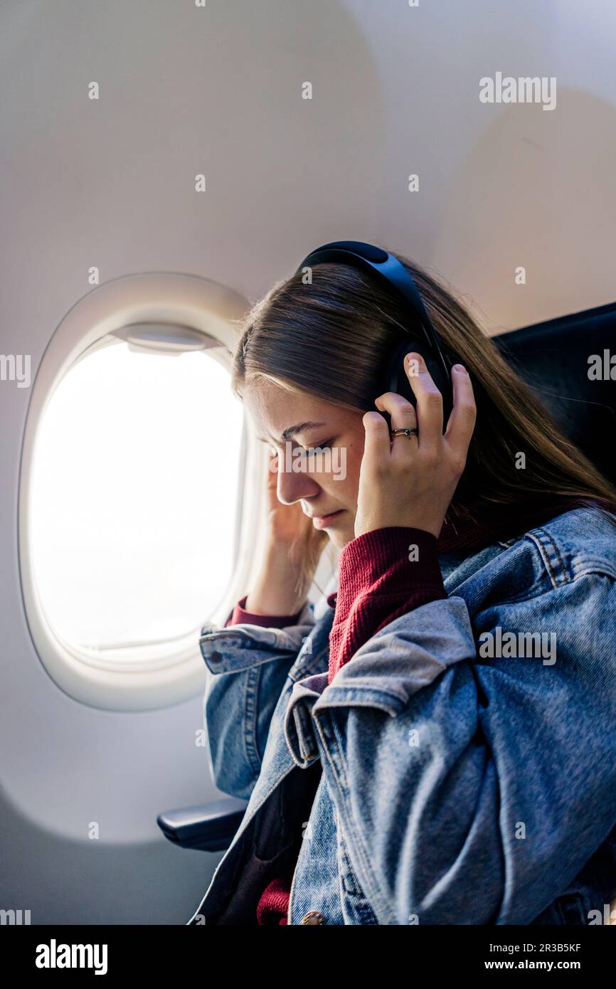 Junge Frau, die im Flugzeug Musik mit Kopfhörern hört Stockfoto