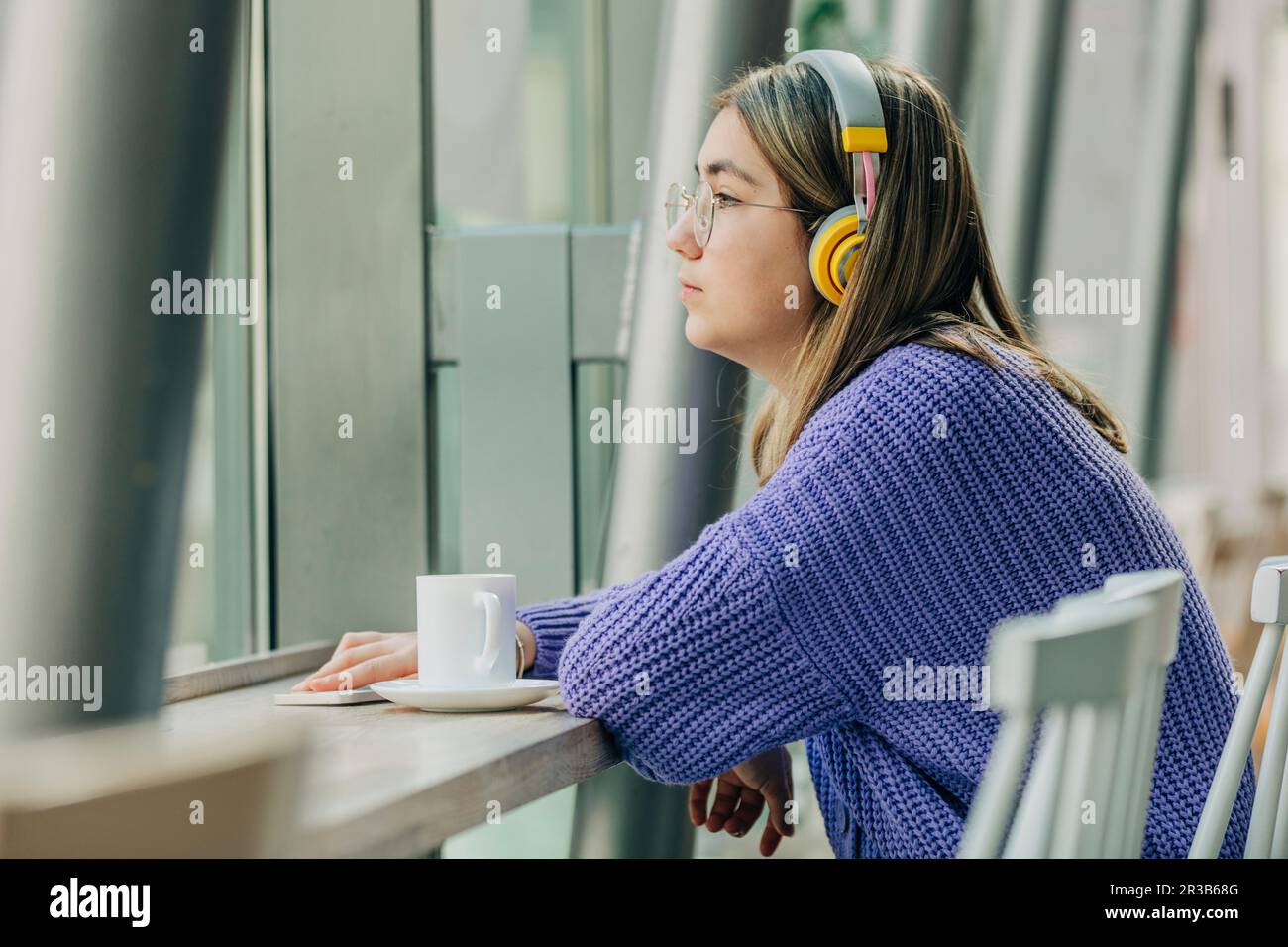 Ein Mädchen mit bluetooth-Kopfhörern träumt in der Schulkantine Stockfoto