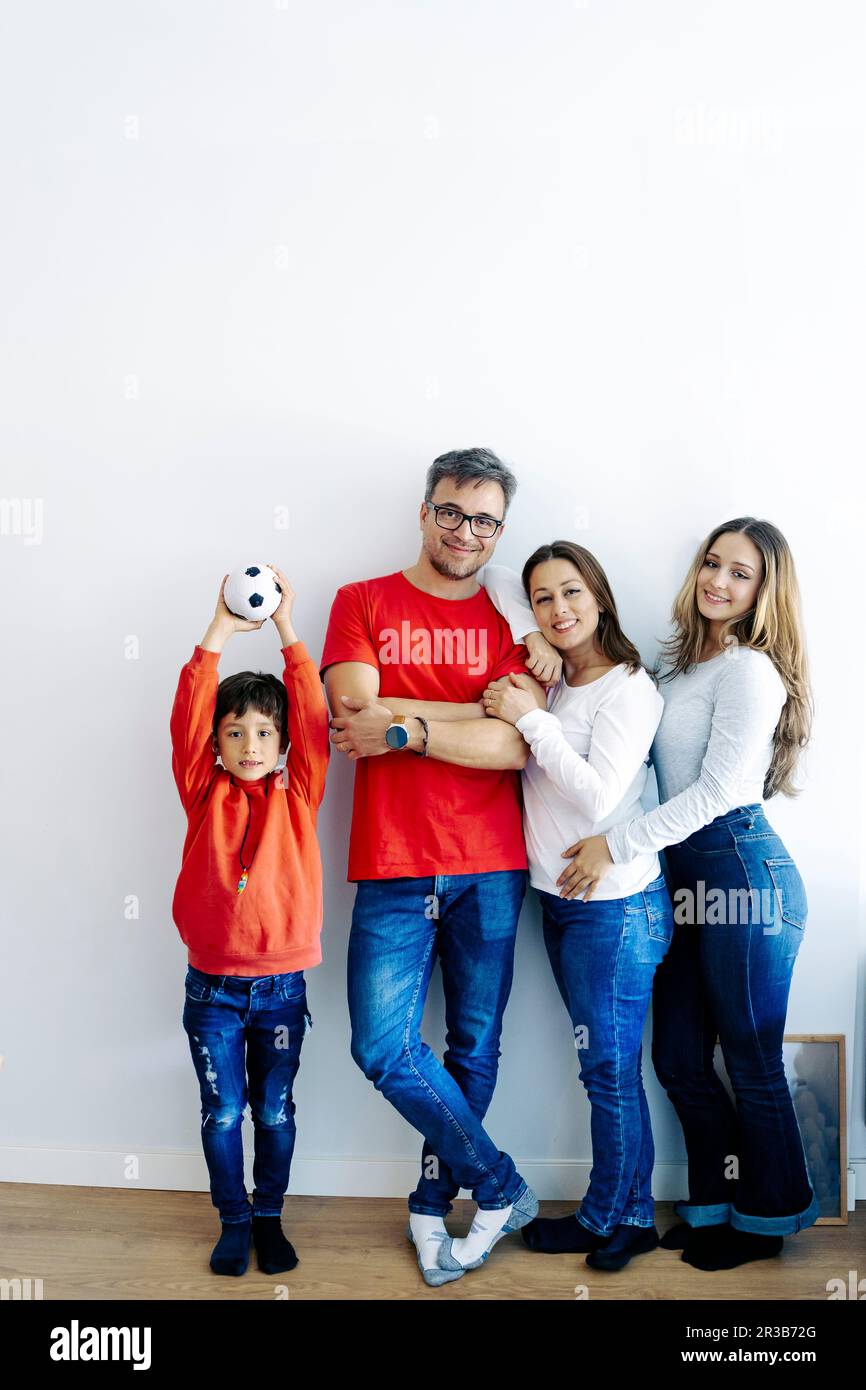 Ein Junge steht mit einem Fußball bei der Familie in der Nähe der Wand zu Hause Stockfoto