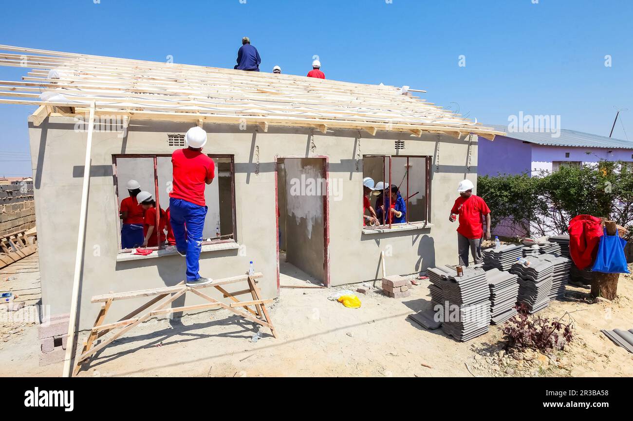 Verschiedene Community-Mitglieder schließen sich den Mitarbeitern von PWC an und bauen ein Billighaus in Soweto Stockfoto