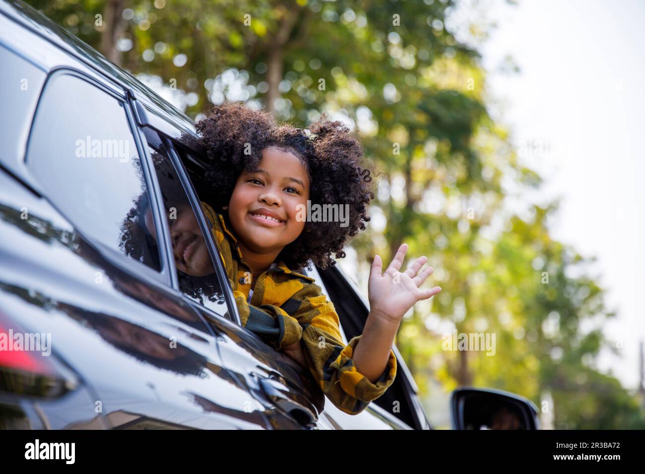 Lächelndes Mädchen, das sich vor dem Autofenster lehnte und winkte Stockfoto